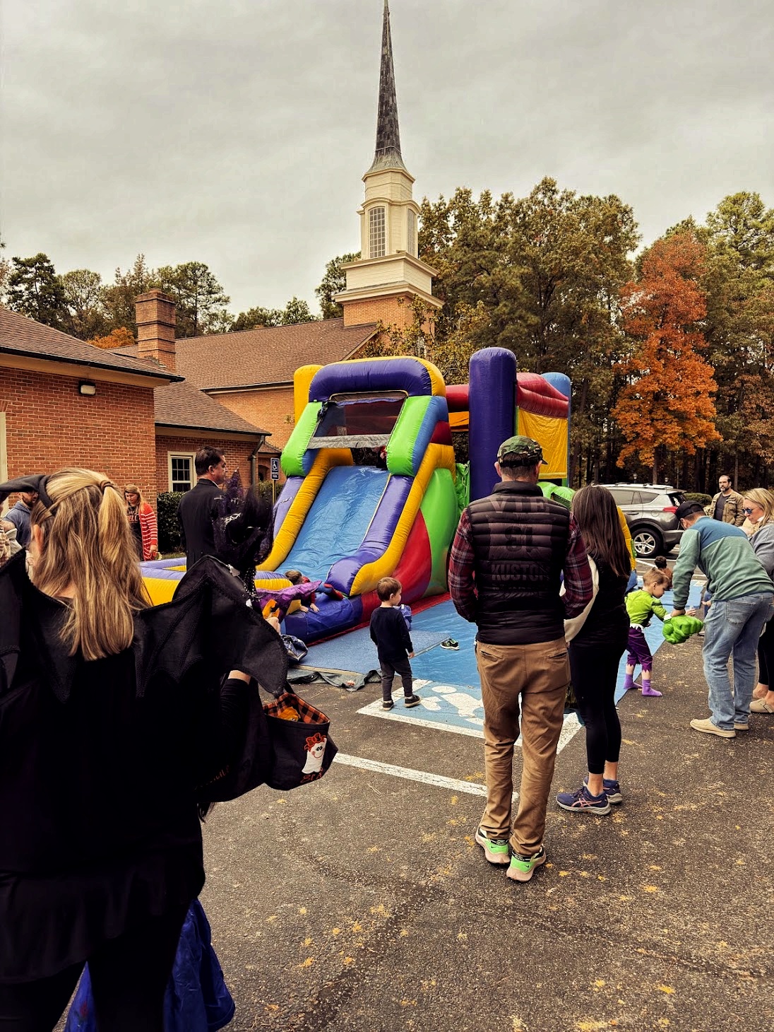 Families gathered in the Welborne parking lot for a fall festival, with the church steeple rising behind an inflatable slide