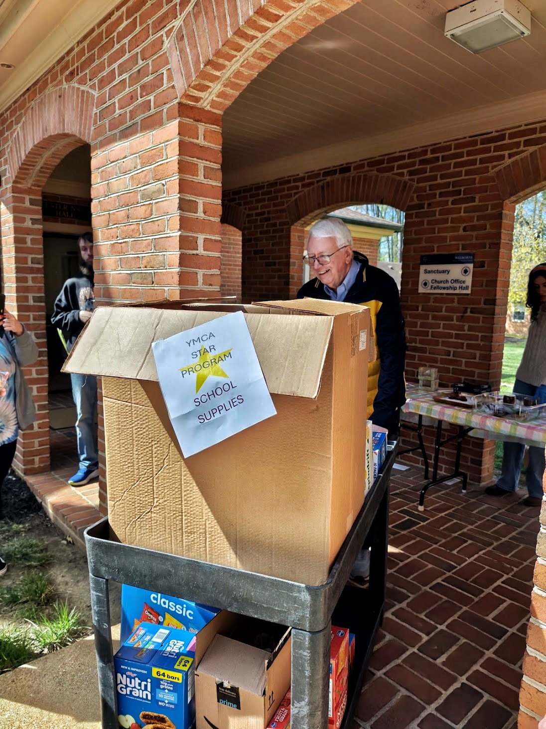 A volunteer moving a cart of donated school supplies on the church porch